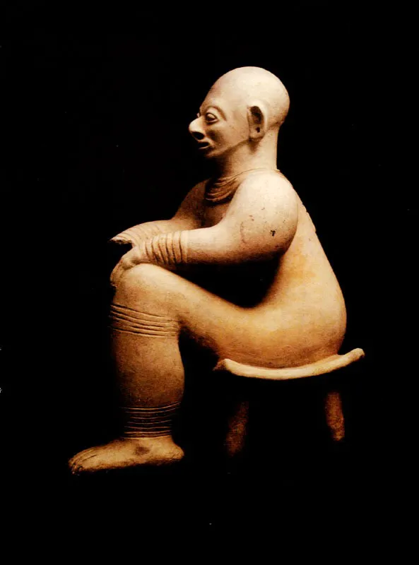 Figura antropomorfa de rasgos hiperrealistas sentada en un dúho tetrápode.