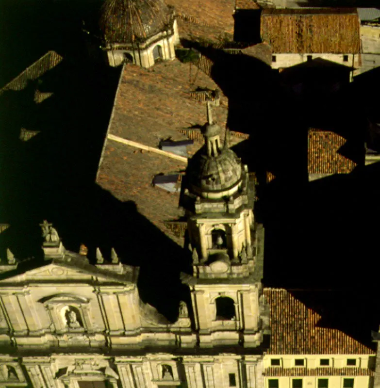 Detalle del frontn, la torre y la cpula de la Catedral Primada. La primera catedral de Bogot se inaugur en mayo de 1572 y sustituy la iglesia primitiva, que dos aos antes se haba desplomado. La segunda catedral, edificacin de un piso, de teja de barro, prest sus servicios religiosos hasta 1807, cuando fue demolida. En febrero del mismo ao se inici la construccin de una nueva catedral, de grandes dimensiones, con planos del arquitecto capuchino fray Domingo de Petrs, a cuyo fallecimiento, en 1811, continu y finaliz la obra en 1823 el maestro artesano Nicols Len. La restauracin de las torres de acuerdo con los planos originales fue efectuada, en 1938, por el arquitecto espaol Rodrguez Orgaz. 