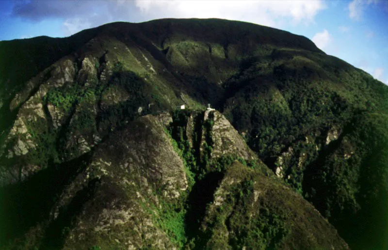 Cruz de La Pea sobre los cerros orientales. El 1 de agosto de 1658, cuenta Guillermo Hernndez de Alba, Bernardino de Len, infortunado buscador de tesoros, al llegar jadeante a un alto picacho de los cerros orientales de Bogot, fue sorprendido y ofuscado por mltiples resplandores que brotaban de una roca. Trep hasta ella, para encontrarse con la visin de una virgen que en sus brazos tena un nio que empuaba una granada, acompaados de San Jos y de dos ngeles de extraordinaria belleza. Regres a la ciudad medio enloquecido llevando a todas partes la nueva de su hallazgo ❏ El domingo de carnestolendas del ao siguiente se echaron los cimientos de la primera ermita que se pretendi edificar en el picacho de la aparicin, sealado hoy con una cruz monumental. 