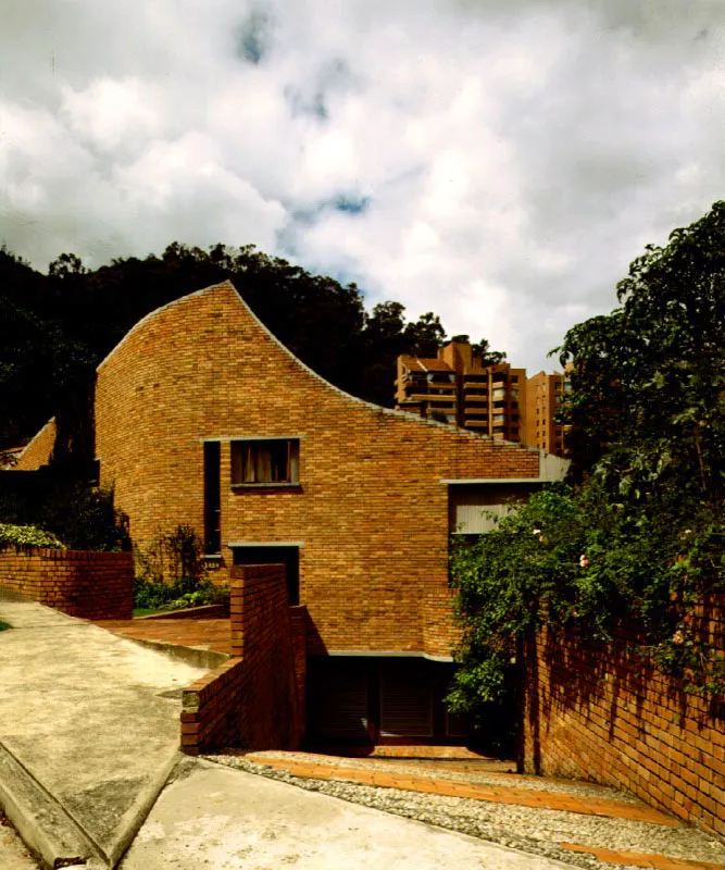 La forma exterior de la casa contradice cualquier imagen preestablecida y enuncia algunas de las intenciones que modelan el espacio interior. La sinuosa figura y la solidez del muro de fachada, con su curvatura y su traza irregular, apenas se afecta con unas pequeñas aberturas. /
Bogotá, D.C. Arquitectos, Fernando Martínez, Guillermo Avendaño.