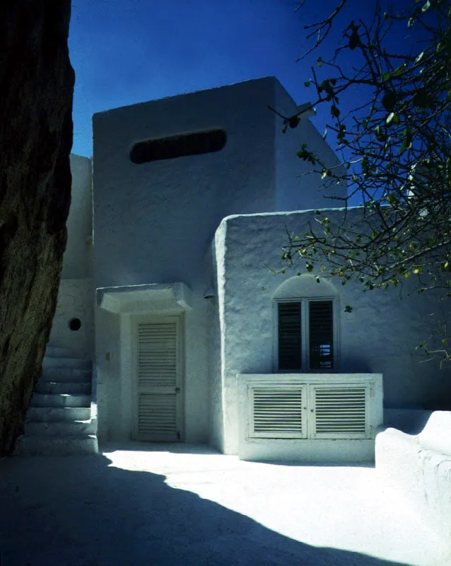 Las blancas masas y formas de los volúmenes contrastan con lo agreste del paisaje. La memoria de la arquitectura del Mediterráneo, evidente en este caso, acentúa el contrapunto entre las formas, colores y texturas de la casa y las rocas tras las cuales parece querer ocultarse. El balcón, apoyado en una de las rocas, es una mínima incursión de la geometría. / Santa Marta, Magdalena. Arquitecto, José María Obregón.