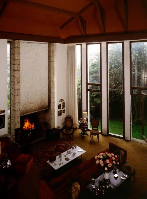 Las dos caras del espacio muestran un tratamiento diferente. Hacia el frente las líneas verticales rítmicamente dispuestas de las ventanas y de la chimenea enfatizan su altura. Hacia el fondo, las superficies cerradas de los muros forman cavidades que se yuxtaponen y cuyo uso y amoblamiento provee texturas y colores diferentes. / Bogotá, D.C. Arquitecto, Enrique Triana Uribe.