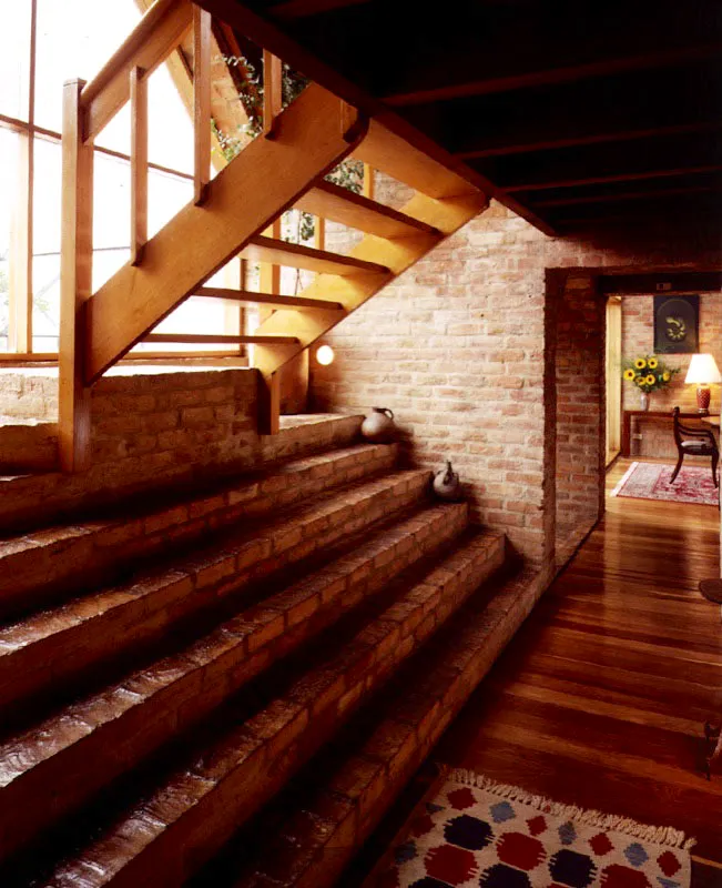 La escalera deja de ser un objeto y se convierte en espacio. La resolución simétrica ¿o asimétrica? del primer tramo evita la imagen convencional de una escalera y afirma la invitación a subir. La partición simétrica ¿o asimétrica? del espacio mediante la ventana opera como línea divisoria entre el estar y el mirar. / Bogotá, D.C. Arquitecto, Herbert Baresch.
