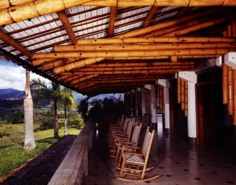 El corredor y el alero propios de la arquitectura tradicional de la región cafetera central se fusionan aquí en un solo espacio cuya cubierta se sostiene en los enormes voladizos logrados con la estructura de guadua. Por su dimensión y proporciones, este espacio se presta tanto para la reunión como para la simple contemplación del paisaje. / Manizales, Caldas. Arquitecto, Simón Vélez.