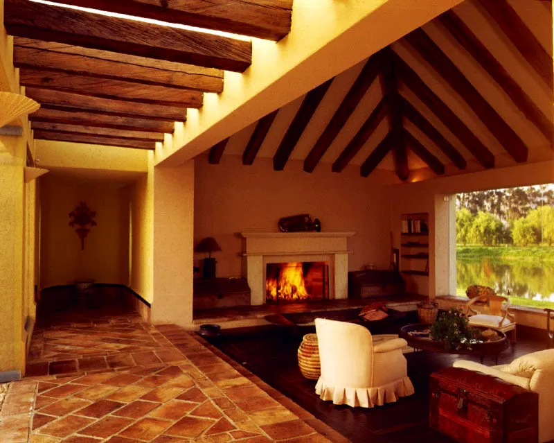 La estructura de la cubierta a la vista y el tratamiento de la chimenea enfatizan la reminiscencia de lo tradicional en el interior de la casa. El gran ventanal con su transparencia ininterrumpida hace el papel de un gran cuadro lleno de naturaleza. / Suesca, Cundinamarca. Arquitecto, Felipe Londoño.