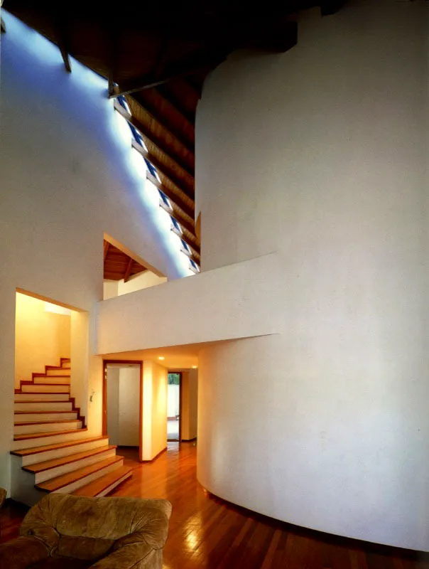 La forma y la elaboración de la cubierta, cuya espiral ascendente remata en un borde de luz, define diferentes escalas en el espacio que cobija. El carácter dinámico impreso por la combinación de la curva y el ascenso en altura, conduce la mirada y el recorrido hacia una compleja intersección de formas. / Envigado, Antioquia. Arquitectos, Alejandro Echeverri, Juan Bernardo Echeverri.