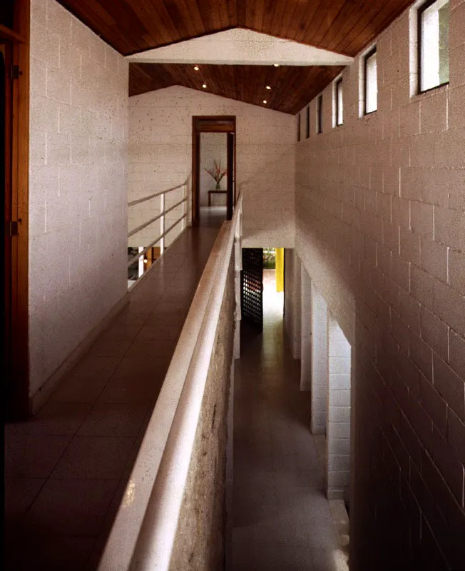 Un corredor-puente, el elemento articulador de la casa, permite configurar espacios de diferente altura e integrarlos en una secuencia. El color blanco aplicado a las superficies construidas en bloque de cemento suaviza su textura sin perderla del todo. / Girardot, Cundinamarca. Arquitecto, Luis Manuel Briceño.