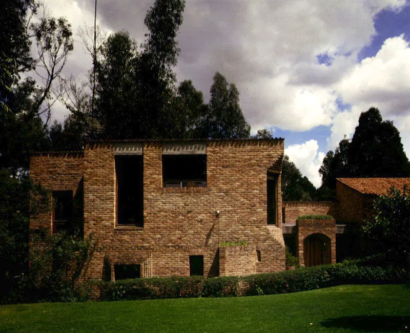 El exterior de la casa muestra toda suerte de incidentes que quiebran sus aristas y sus planos y que responden a intenciones precisas de relación del interior con su entorno. La ventana localizada al fondo del salón contradice la tradición del muro cerrado de fondo. La precisión en el ajuste de la ventana y el desvanecimiento de sus marcos crea la ilusión de una total transparencia e introduce la naturaleza dentro del salón. / Bogotá, D.C. Arquitectos, Jorge Rueda, Carlos Morales.