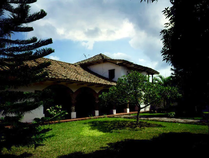 Casa de Guacarí,
Valle del Cauca.
En rigor, no es actualmente una construcción rural,
ni lo que hoy existe corresponde a la primera sede de la hacienda de este nombre. Es posible que algunos de los componentes arquitectónicos de la casa original hayan sido incorporados a lo actual, construida cuando el caserío de Guacarí creció en torno a la hacienda fundada en el siglo XVII, y se hizo necesario levantar una iglesia propia del lugar. Al comenzar el siglo XIX la edificación pasó a ser casa cural. Los espacios libres circundantes, singulares en un núcleo urbano, son propios de una casa
de finca o hacienda.
Si el volumen realzado del piso alto es característico de las casas rurales de la región, la reciente restauración de la casa dejó al desnudo los atípicos arcos rebajados en ladrillo de las galerías del piso bajo, en un equívoco acento decorativo.