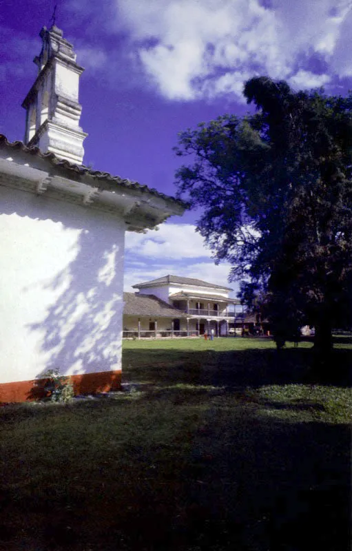 La Concepción de Amaime. El Cerrito, Valle del Cauca.
Es la casa de hacienda arquitectónicamente más singular y destacada de la región. Llega a su forma “final” en la segunda mitad del siglo XVIII. Se destaca su volumetría en un
lugar llano, topográficamente indiferente, por lo que depende de su propia arquitectura para cualificar los espacios en torno suyo. Posee además de la casa de los señores, de planta compacta, una capilla exenta, una ramada (vivienda de peones y depósitos), y tuvo también el tradicional baño al aire libre y un extenso acueducto del cual quedan algunos rastros. A cierta distancia de la casa subsiste el trapiche azucarero. La localización de la capilla y el volumen sobreelevado del extremo occidental de la casa, provisto de un balcón alto y galería baja con columnas talladas, conforman un conjunto arquitectónico de espléndida calidad.