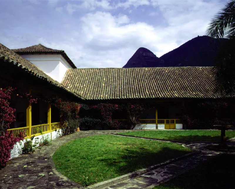 Aposentos, Simijaca, Boyac.
Las generosas proporciones del 
patio principal de Aposentos, reflejan su origen terico. 
Ntese el contraste que ofrece este patio con el de la casa de Gotua, Iza, Boyac. Ambos obedecen al mismo concepto de ordenacin espacial 
y fueron construidos con idnticos materiales y mtodos constructivos, pero los resultados ambientales son muy distantes entre s. Uno se hizo simplemente para vivir, el otro para contemplar su elegancia formal.
La inevitable intervencin de 
poca republicana 
en la casa (cielos rasos planos, enchapado 
y molduracin de columnas en madera, colocacin de barandas sobre los poyos hacia 
el patio, etc.) afect marginalmente la calidad ambiental de los espacios. Ntese cmo la presencia dominante de los tejados artesanales parece pertenecer a 
un mundo conceptual muy diferente de la ortodoxia modular 
de las columnatas en torno al patio o la ordenacin de la fachada principal 
de la casa, como 
si sta hubiese sido pensada para ser cubierta con terrazas planas, a la manera de la provincia valenciana de donde era oriundo el autor de la casa, Fray Domingo de Petrs. 