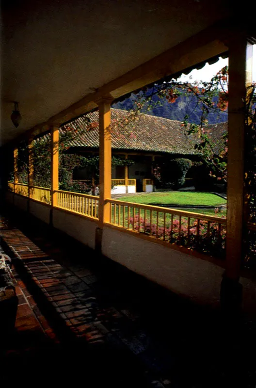 Aposentos, Simijaca, Boyacá.
Las generosas proporciones del
patio principal de Aposentos, reflejan su origen teórico.
Nótese el contraste que ofrece este patio con el de la casa de Gotua, Iza, Boyacá. Ambos obedecen al mismo concepto de ordenación espacial
y fueron construidos con idénticos materiales y métodos constructivos, pero los resultados ambientales son muy distantes entre sí. Uno se hizo simplemente para vivir, el otro para contemplar su elegancia formal.
La inevitable intervención de
época republicana
en la casa (cielos rasos planos, enchapado
y molduración de columnas en madera, colocación de barandas sobre los poyos hacia
el patio, etc.) afectó marginalmente la calidad ambiental de los espacios. Nótese cómo la presencia dominante de los tejados artesanales parece pertenecer a
un mundo conceptual muy diferente de la ortodoxia modular
de las columnatas en torno al patio o la ordenación de la fachada principal
de la casa, como
si ésta hubiese sido pensada para ser cubierta con terrazas planas, a la manera de la provincia valenciana de donde era oriundo el autor de la casa, Fray Domingo de Petrés.