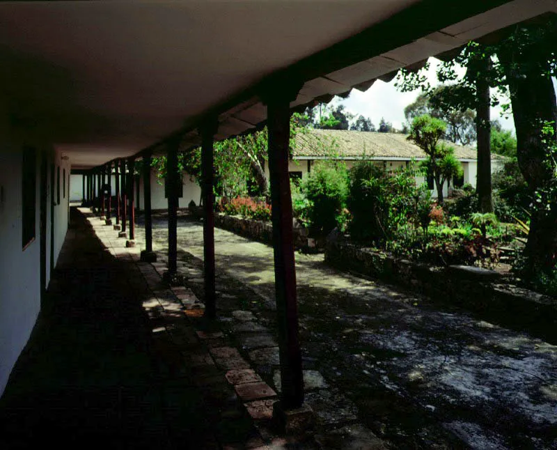 Yerbabuena, La Caro, Chía, Cundinamarca. Parece ser que los tramos originales
de la casa de Yerbabuena, formando una “L”
en dos costados del patio interior,
fueron edificados al final del siglo XVIII, cuando la dehesa de Hatogrande fue desmembrada y surgieron varias haciendas a raíz de tal subdivisión. Ya en la primera mitad del siglo XIX la casa fue sucesivamente
ampliada y reformada hasta adquirir una extensión insólita entre sus congéneres sabaneros. En la segunda mitad
del siglo XIX la republicanización de Yerbabuena le dio el tono arquitectónico que hoy, redecorado considerablemente varias veces, es visible en el tramo más “moderno” de la casa, (arriba) incluyendo cerramientos de galerías en vidrieras
“a la francesa” y rejas pseudo-sevillanas de hierro. Los aleros “de caja” usuales en las casas de hacienda caucanas, pero insólitos en plena Sabana de Bogotá y visibles aquí en las fachadas y hacia el patio interior, le fueron impuestos a la casa al final de la década de los cuarenta.