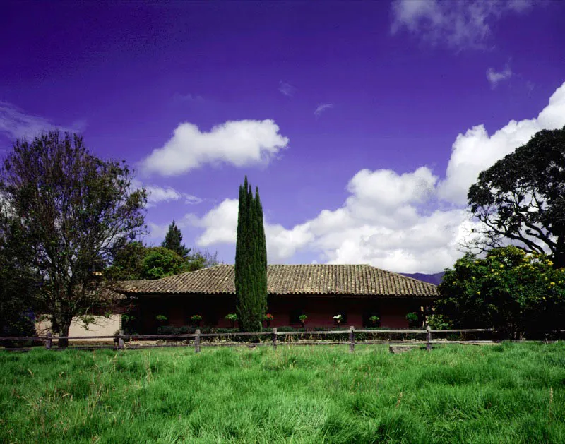 La Esmeralda, Tabio, Cundinamarca.
Forma parte de las
edificaciones rurales creadas al final de la época colonial, cuando se intensificó la desmembración de los latifundios en la sabana de Bogotá. La enorme propiedad de El Novillero, se dividió en algún momento de su historia en once fracciones, una de
las cuales llegó
a ser La Esmeralda. Aunque el tamaño y época de construcción puedan variar mucho de una casa de hacienda a otra, la gracia de los tejados o la delicada relación entre casa y lugar son constantes en todas. En La Esmeralda el prisma imaginario de espacio en el cual se inscribe la casa es casi tangible, y la casa misma podría ser tan natural como sus árboles.