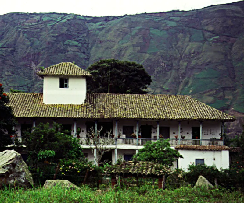 Bombon, Nario.
Se sita en una regin montaosa donde las haciendas fueron escasas pero notablemente extensas. Pocos latifundios del sur del pas llegaron a tener casas de cierta importancia arquitectnica y aun menos de ellas sobrevivieron hasta el siglo actual. De ah el carcter excepcional de Bombon. Para su construccin debi ser necesario recorrer infinidad de veces las leguas que separan su localizacin del punto ms prximo donde era posible obtener teja de arcilla, buen adobe y ante todo, buena cal. Y devastar, de paso, una enorme rea de bosques para sacar de ellos las gruesas columnas, dinteles y soleras que conforman la recia estructura de cubiertas y galeras de la casa. 
Al ver una casa de hacienda en un paraje remoto, se tiende a olvidar el esfuerzo fsico y tecnolgico que su construccin supone y que califica decisivamente su arquitectura.
Izquierda, El mirador atpico que rompe la unidad volumtrica de los tejados. Se requiere muy poco para alterar la continuidad y la armona formal de los tejados coloniales. Esta atalaya, indispensable para la vigilancia de la comarca circundante en una regin de larga y difcil historia de contiendas militares y azarosa existencia cotidiana, es una adicin de la primera mitad del siglo XIX, no un rasgo original de la edificacin colonial de mediados del siglo XVIII. 