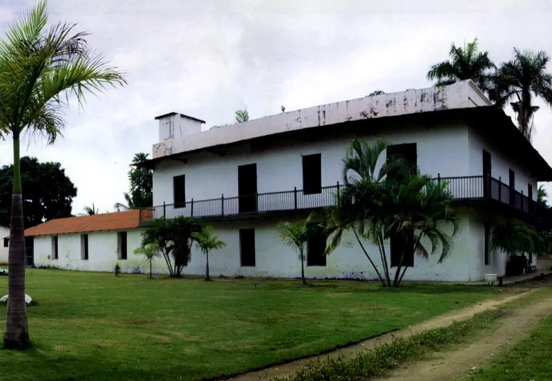 Papare, Ciénaga, Magdalena.
Al extremo opuesto
de la geografía colombiana, la casa
de hacienda de trapiche de Papare, Magdalena, es un ejemplo tan excepcional y aislado como Bomboná.
Las técnicas constructivas presentes en casas urbanas de Santa Marta y Ciénaga fueron obviamente utilizadas en Papare, incluyendo las cubiertas en terrazas planas con áticos, lo cual la hace análoga a San Pedro Alejandrino, localizada en la misma región. Sólo estos dos ejemplos de las regiones costeras del Caribe se apartan de la omnipresencia de tejados en las casas rurales ilustradas en este volumen. Papare tiene, además, un innegable aspecto de casa urbana debido al uso de balcones perimetrales voladizos, en lugar de amplias galerías sobre columnas o pies derechos de madera. Aquéllos semejan, en la independencia entre piso de balcón y tejadillo, los que aparecen durante el siglo XIX en todas las ciudades costeras del Caribe.