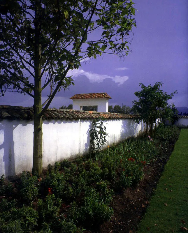 , Casa de
Antón Moreno,
Popayán, Cauca.
La más bella e inspirada relación de casa y paisaje entre las haciendas próximas a Popayán es sin duda la de Antón Moreno. La singular mezcla de dureza y suavidad de la arquitectura de la casa es la que presenta el paisaje circundante, y la una surge y depende de lo otro. Alcanzó su forma durante la última década del siglo XVIII, luego de terremotos y reformas sin cuenta, aunque la hacienda existía como “de trapiche” al final del siglo anterior, pasando luego a ser ganadería.
Antón Moreno es una síntesis de los esquemas básicos de ordenación espacial más usuales en la arquitectura de las casas de hacienda neogranadinas. Combina con elegancia un patio principal, atravesado por una rama sobre arquillos del complejo acueducto
–de raigambre islámica– de la casa, con galerías exteriores abiertas al panorama circundante. Incluye una capilla anexa ligada a la casa por el tramo que alberga las dependencias de servicios. Para estar a tono con la modestia arquitectónica de su espacio, la capilla posee un singular retablo pintado en falso relieve sobre lienzo.