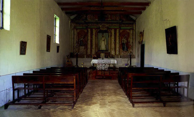 , Casa de
Antón Moreno,
Popayán, Cauca.
La más bella e inspirada relación de casa y paisaje entre las haciendas próximas a Popayán es sin duda la de Antón Moreno. La singular mezcla de dureza y suavidad de la arquitectura de la casa es la que presenta el paisaje circundante, y la una surge y depende de lo otro. Alcanzó su forma durante la última década del siglo XVIII, luego de terremotos y reformas sin cuenta, aunque la hacienda existía como “de trapiche” al final del siglo anterior, pasando luego a ser ganadería.
Antón Moreno es una síntesis de los esquemas básicos de ordenación espacial más usuales en la arquitectura de las casas de hacienda neogranadinas. Combina con elegancia un patio principal, atravesado por una rama sobre arquillos del complejo acueducto
–de raigambre islámica– de la casa, con galerías exteriores abiertas al panorama circundante. Incluye una capilla anexa ligada a la casa por el tramo que alberga las dependencias de servicios. Para estar a tono con la modestia arquitectónica de su espacio, la capilla posee un singular retablo pintado en falso relieve sobre lienzo.