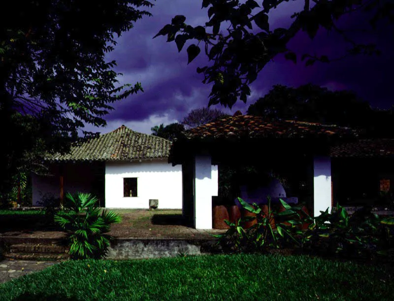 Piedechinche, El Cerrito, Valle del Cauca.
(Actual Museo de la Caña).
Las haciendas del Valle del Cauca fueron divididas en dos géneros, ya bien entrada la Colonia, para la implantación del cultivo de la caña de azúcar asiática en la región. Las haciendas productoras de azúcar pronto superaron en rendimiento a las de ganado vacuno. Algunas de las más prominentes haciendas de trapiche de la región, como El Alisal, han sido destruidas recientemente. Piedechinche pasó a una existencia, preferible a la desfiguración modernizante o la demolición, como museo histórico de
una actividad agrícola regional, con el mérito de hacer visible la organización espacial de una industria adscrita a una casa de hacienda.
Nótese cómo la casa
de los señores de Piedechinche ofrece similaridades espaciales con haciendas caucanas como Coconuco, Pisojé o Yambitará. Tales como la sobre-elevación de un tramo a manera de mirador y el uso de galerías exteriores de gran amplitud en piso alto y bajo, sin abarcar la totalidad de las fachadas.
