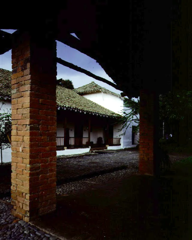 Piedechinche, El Cerrito, Valle del Cauca.
(Actual Museo de la Caña).
Las haciendas del Valle del Cauca fueron divididas en dos géneros, ya bien entrada la Colonia, para la implantación del cultivo de la caña de azúcar asiática en la región. Las haciendas productoras de azúcar pronto superaron en rendimiento a las de ganado vacuno. Algunas de las más prominentes haciendas de trapiche de la región, como El Alisal, han sido destruidas recientemente. Piedechinche pasó a una existencia, preferible a la desfiguración modernizante o la demolición, como museo histórico de
una actividad agrícola regional, con el mérito de hacer visible la organización espacial de una industria adscrita a una casa de hacienda.
Nótese cómo la casa
de los señores de Piedechinche ofrece similaridades espaciales con haciendas caucanas como Coconuco, Pisojé o Yambitará. Tales como la sobre-elevación de un tramo a manera de mirador y el uso de galerías exteriores de gran amplitud en piso alto y bajo, sin abarcar la totalidad de las fachadas.