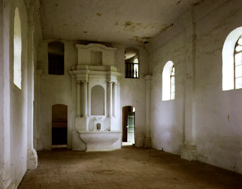 Saldaña, Capilla aislada, Saldaña, Tolima.
La razón de ser de las capillas anexas, exentas o aisladas en las casas rurales neogranadinas, era la necesidad de proveer el culto religioso a feligreses venidos de haciendas, veredas o caseríos vecinos carentes de iglesia, aparte de los residentes y trabajadores de la propia hacienda. En torno a ésta debía existir un espacio adecuado para procesiones y otras ceremonias al aire libre.
La casa de la hacienda Saldaña vino a menos en el siglo XIX y ha perdido grandemente su fisonomía y carácter de época republicana en el XX, pero de la construcción colonial resta aún la capilla, aparentemente construida a fines del siglo XVIII. Sus ingenuos barroquismos, obviamente realizados “a ojo” y de memoria por algún anónimo constructor, se limitan a dos medios óvalos cortados en las diagonales del frontón en fachada, produciendo así una silueta mixtilínea, y en el interior un singular retablo afacetado en mampostería. La capilla de Saldaña es lo que se podría llamar “barroco recóndito rural neogranadino”.