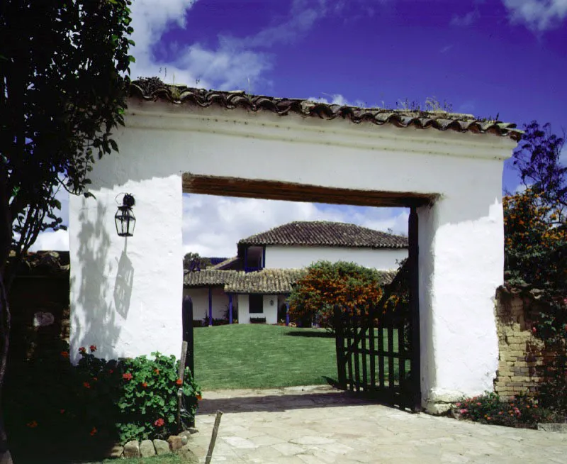 Tilatá Chocontá, Cundinamarca. Datando aparentemente
del siglo XVIII,
Tilatá presenta una atrayente volumetría que indica un crecimiento por etapas. Aunque no
han faltado las inevitables estructuras utilitarias surgidas
al lado de casi todas
las casas de hacienda cundinamarquesas, la casa conserva en gran medida su notable implantación en un territorio aún (1997) no invadido por canteras, fábricas o clubes campestres.
Más importante todavía, aún existe la envoltura espacial de muros y tapias que
es vital complemento de la casa.
