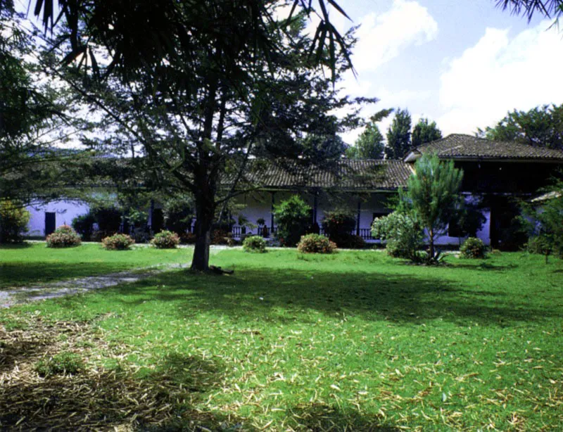 Pisojé, alrededores de Popayán, Cauca. Pisojé está situada en un paraje en el cual se suman prácticamente todos los elementos que conforman el paisaje regional:
suaves colinas, cerros más empinados, un
río adyacente, panorama lejano de cordillera con volcanes y nieves eternas, dramáticas puestas de sol. A fuerza de presenciar una y otra vez el espectáculo de la precisa arquitectura de las casas de hacienda caucanas,
se podría concluir
que ese poético sentido del lugar
que las distingue se tornó en cierto
modo en convencional. El reiterado e invariable acierto de hacendados y constructores en el aprovechamiento de las posibilidades ambientales de los lugares se hizo, al
paso del tiempo, costumbre y tradición.
Pisojé no fue ajeno a las oleadas de vandalismo que recorren de vez en cuando el campo colombiano. Si la
casa ha escapado a
una modernización incurable, la capilla exenta de la casa, similar a las de Antón Moreno y Calibío, fue derribada para instalar en su lugar un “baño” para ganado vacuno, con el argumento de que a menos de media legua de allí estaba la iglesia de La Jimena, y que las almas se salvaban igual si se rezaba en la una o en la otra.
