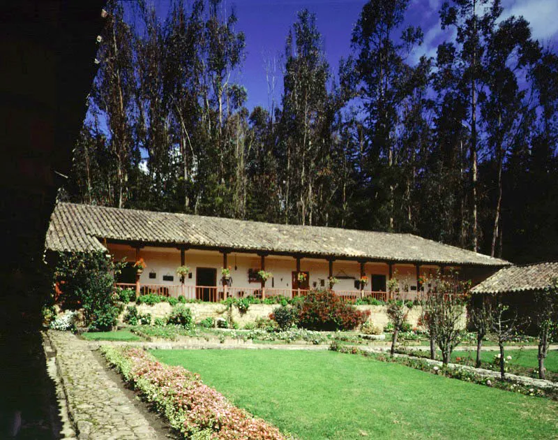 Los Aposentos, Chocontá, Cundinamarca.
Son varias las casas
de hacienda en Cundinamarca que llevan este nombre,
el cual es también frecuente en Castilla
y Andalucía. Al comienzo del siglo XVIII existían haciendas Aposentos
en Simijaca (ilustrada en páginas anteriores), Sopó y Chocontá (la que se muestra aquí),
y otras más aparecieron en la región durante el siglo XIX. Al igual que con Casablanca, la proliferación de ciertos nombres de propiedades rurales tendría las mismas razones que la abundancia de Pedros o Juanes entre los pobladores españoles de la Nueva Granada.
Los Aposentos, de los alrededores de Chocontá, cuya edificación original parece datar de la primera mitad del siglo XVIII, aunque la hacienda misma se conforma a mediados del XVII, carece del tono académico “fuera de serie” de su homónimo de Simijaca y pertenece más al género “clásico” de casa sabanera. Como tal, posee espléndidas proporciones modulares en las columnatas de las galerías visibles aquí, y un delicado “acomodo” al paisaje circundante. Parece ser que la casa original consistía solamente del tramo longitudinal visible a derecha, lo cual asimilaría la casa al tipo de planta compacta con grandes galerías en sus lados longitudinales. Esto corrobora la idea de que no existe una organización espacial de casas de hacienda propia o típica de una región o zona climática en particular, puesto que las casas de planta compacta existen desde el sur
de la Nueva Granada hasta el altiplano cundiboyacense. El crecimiento de la
casa a través de las décadas se ha mantenido afortunadamente dentro de límites volumétricos y una continuidad formal que hacen de Los Aposentos uno de los ejemplos más depurados de casa de hacienda cundinamarquesa.