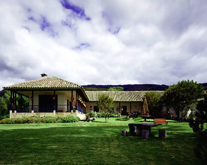San Rafael, Sesquilé, Cundinamarca.
Esta casa, construida al final del siglo XIX se localiza en las proximidades de la de Chaleche, algo más antigua e ilustrada en el Capítulo “Hacienda y Casa”, y corresponde a una de las subdivisiones de época republicana de la hacienda de ese nombre. Desde luego, su atrayente volumetría es una plasmación directa de la de Casablanca, Sopó, y otras casas coloniales de la sabana de Bogotá, pues no habría razón para “inventar” una arquitectura diferente con la cual enfrentar el paisaje
de la región o simplemente instalar una buena casa rural en un altozano adosado a los cerros vecinos.