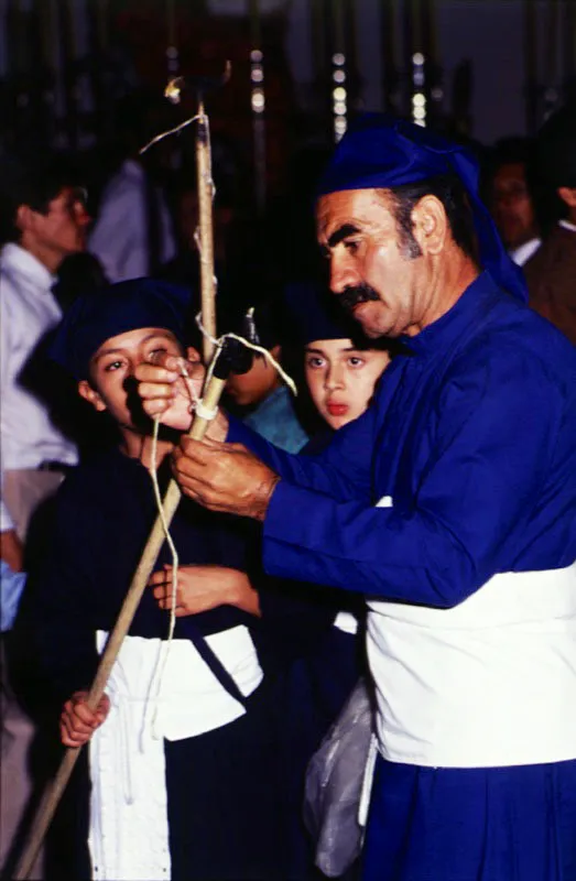 Un carguero veterano le colabora a un pequeo "moquero" en la preparacin de su herramienta. Los moqueros son nios encargados de quitarles a las velas los chorriones de cera, llamados popularmente "mocos". 