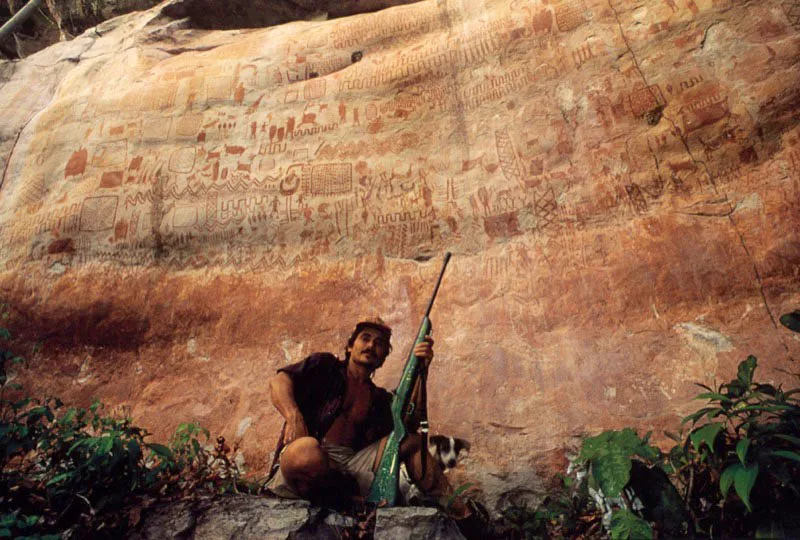 Memorias
pictográficas de la Amazonia
son el telón de fondo para el nuevo
capítulo de la selva, que impone otros símbolos
animales en la escopeta del cazador, mientras su perro,
Peligro, se asoma a la escena rupestre del Guaviare. Aunque
el documento en piedra aún esté intacto, a pesar de la deforestación
y las quemas en torno, otras pinturas indígenas han sido allí vandalizadas
con grafiti sobrepuesto a esta génesis del arte neotropical: una escritura sagrada
que permaneció incólume al paso del tiempo, hasta la llegada del hombre “letrado”. Aldo Brando