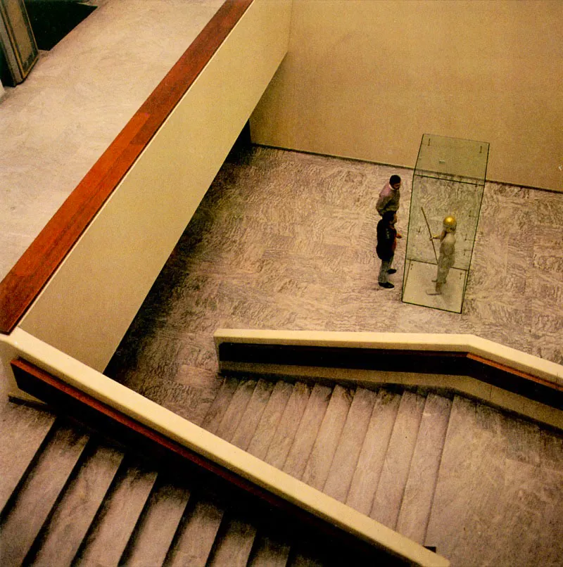 Vista de la escalera de acceso a las 
	distintas secciones del Museo. Dentro de 
	la vitrina se aprecia el Anfitrin, adornado con piezas de oro, quien recibe	a los visitantes.
 