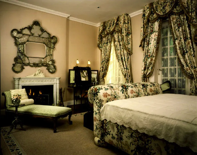 El romántico dormitorio principal exhibe chintz de begonias en la cama, hecha por encargo, y las cortinas, un espejo veneciano sobre las paredes tapizadas, así como la combinación de una mesa de tocador estilo George III con una silla arpa estilo Charles X.