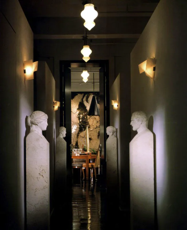 Flanqueado por una colección de estatuas italianas, este corredor lleva a la oficina privada de Montoya. Los apliques de las paredes en alabastro son de Pierre Chareau. La escala de las puertas acentúa el tono dramático de anticipación.