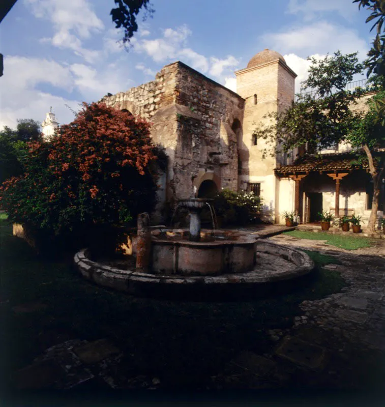 Exterior del jardín de una casa antigüeña restaurada, que conserva los muros originales de piedra.