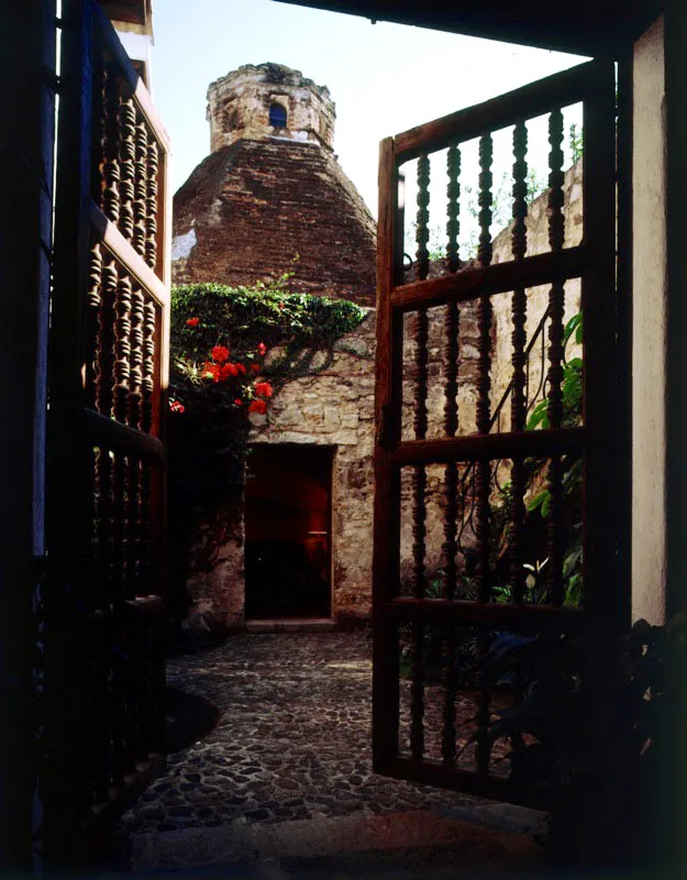 Pequeño patio interior de piedra en una casa restaurada de Antigua, con vista a la vieja cocina de chimenea en forma de cúpula y acceso desde una puerta de bolillos de madera.