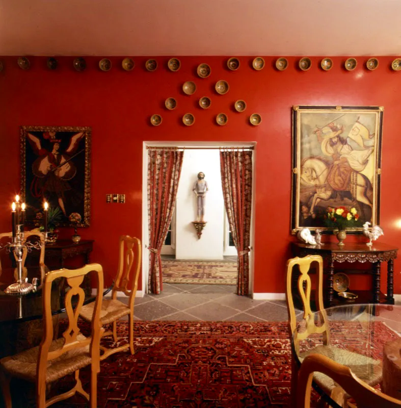 Comedor de casa contemporánea en ciudad de Guatemala, con piezas de mayólica antigüeña sobre el muro; al fondo, en el corredor, una escultura de vestir colonial.