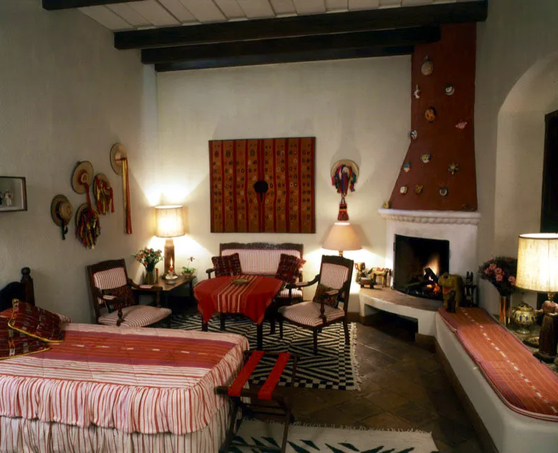 Dormitorio de una casa restaurada en Antigua, donde se unen colores y formas: el blanco del muro, el rojo terroso de la chimenea con máscaras de coco sobrepuestas, el textil indígena en que domina el rojo y el café del “cuyuscate” (algodón), y un sombrero chamula chiapaneco.