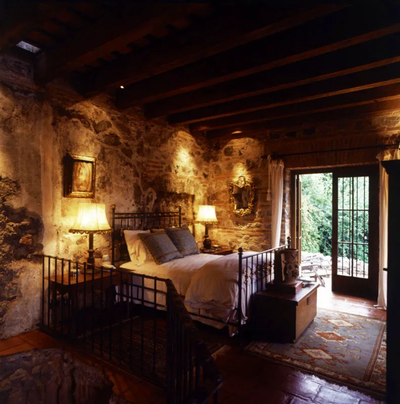 Dormitorio de una casa antigüeña restaurada, con los muros originales, sin revoque y cama de hierro forjado.