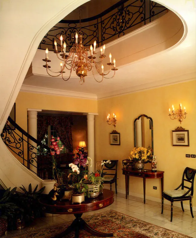 Vestíbulo de una casa contemporánea, con escalera circular, baranda de hierro forjado y araña de bronce.