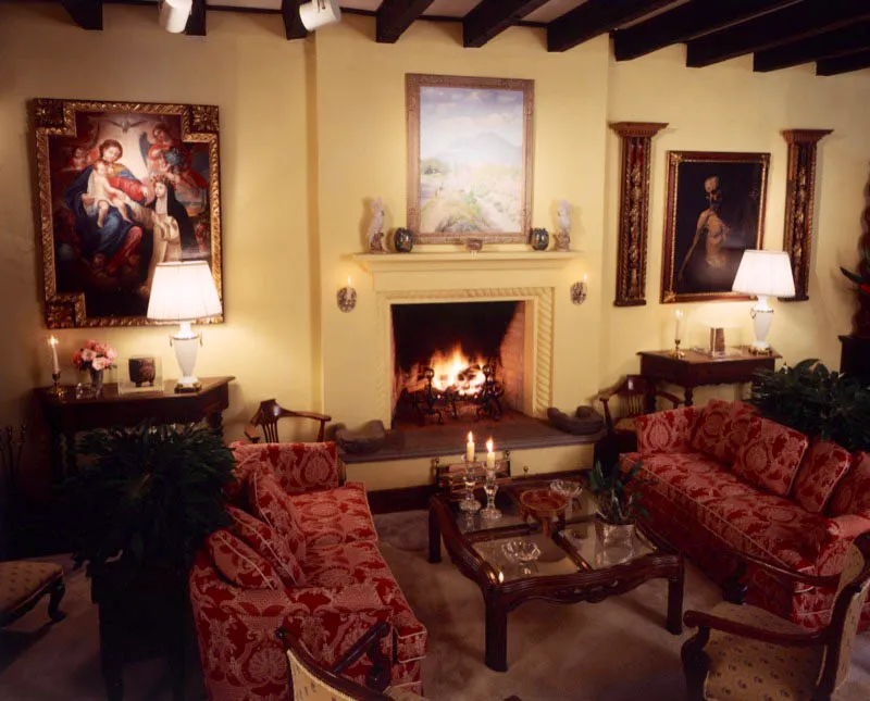 Salón principal de una casa contemporánea de Antigua, con muros pintados en amarillo claro, una chimenea moderna, sobre la cual cuelga un óleo del pintor guatemalteco contemporáneo José Luis Álvarez, y a los lados dos pinturas de autores desconocidos: una de Santa Rosa de Lima venerando a la Virgen y otra de un personaje con el torso desnudo, entre dos relieves barrocos.