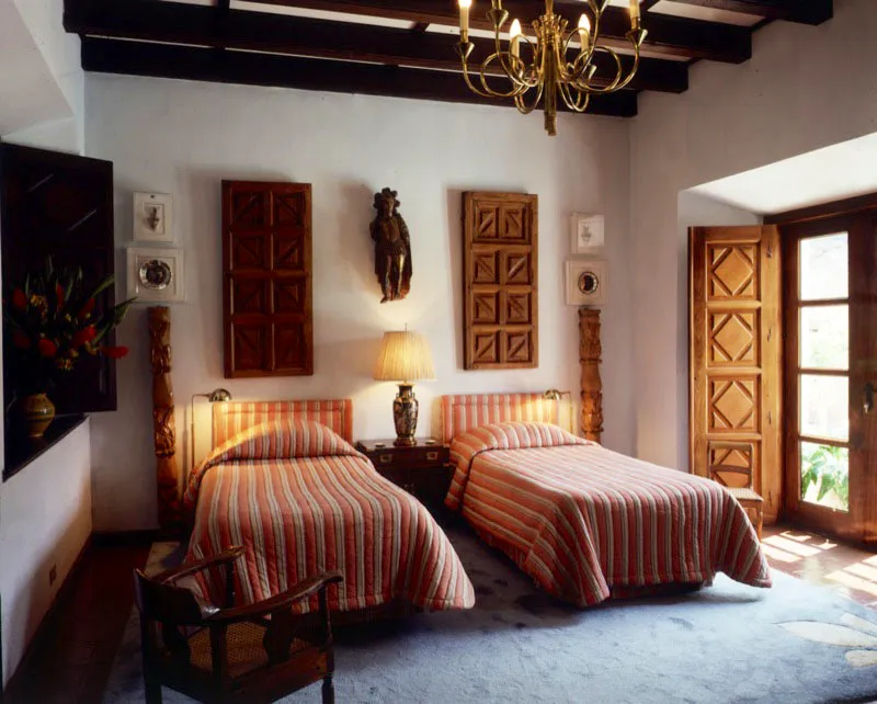 Dormitorio tradicional de una casa de Antigua, decorado con puertas talladas sobrepuestas y columnas coloniales a los costados de las camas.