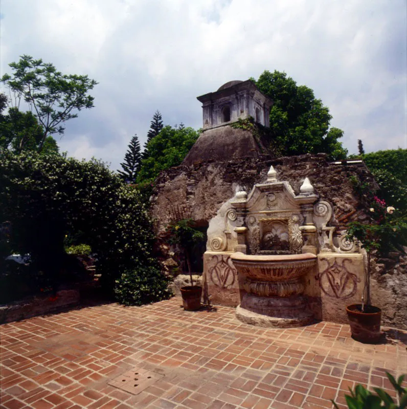 Fuente colonial de piedra repellada, con bcaro de estilo primitivo, en Antigua. Detrs, cpula de la cocina colonial de la casa original.  