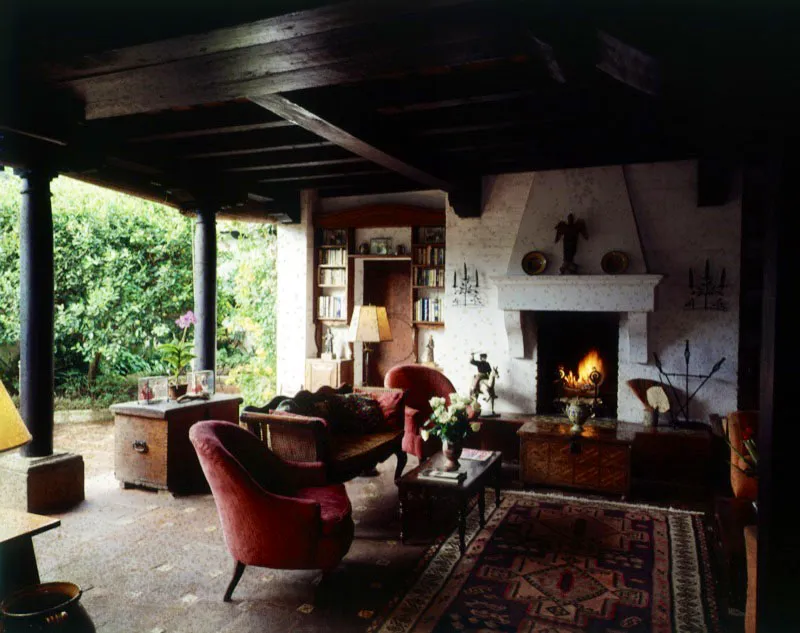 Sala de una casa antigea abierta a un patio interior, con piso de baldosa salpicado de azulejos. Sobre la chimenea, una escultura primitiva de un ngel en madera y dos platos de maylica local; sobre la pared, a ambos lados, candeleros modernos de hierro forjado, adelante un bal de madera incrustada de diseo geomtrico, trabajo tradicional de la Antigua.  