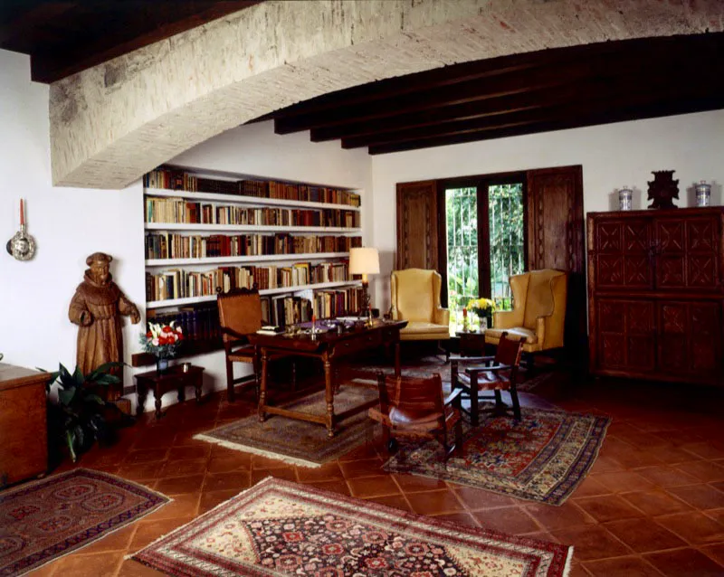En este estudio-biblioteca de casa contemporánea en Antigua, se combinan las estanterías del fondo, con un escritorio antiguo y un aparador tallado. Bajo el gran arco rebajado de ladrillo expuesto, que contrasta con la baldosa en barro cocido del piso, una escultura colonial en madera de cedro encerada.