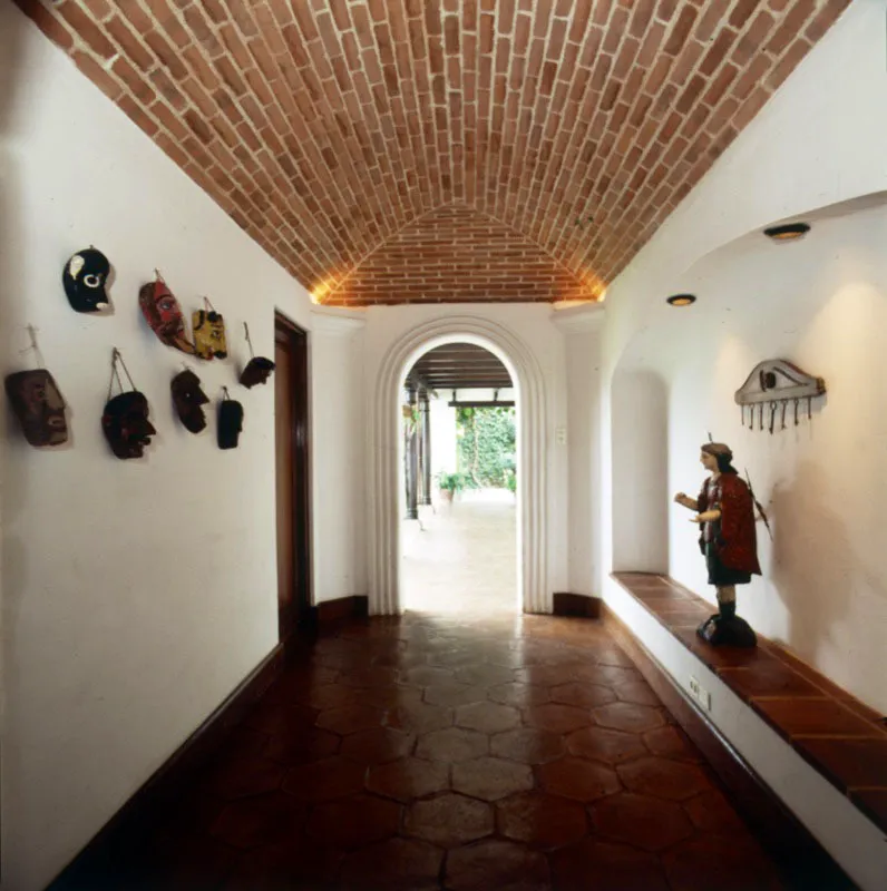 Pasillo de una casa contemporánea en Antigua, donde se logra un ambiente interesante gracias a la bóveda con el ladrillo visto. En el muro izquierdo, ocho máscaras indígenas de danzas tradicionales; a la derecha,
sobre el banco, un arcángel policromado, escultura popular.