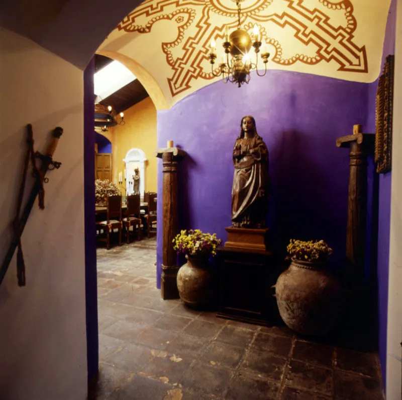 Pasillo abovedado de acceso al comedor de la casa, pintado a mano. El añil del muro sirve de fondo a dos vasijas de cerámica popular con flores, dos columnas de madera y una escultura mariana sin estofado en el centro.