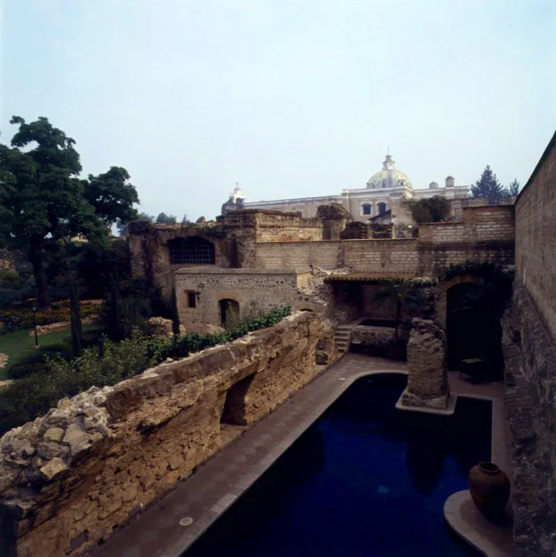 Piscina desarrollada entre la ruina, conectada con el jardín lateral a través de un muro colonial en piedra. Al fondo las cúpulas de la ciudad colonial.