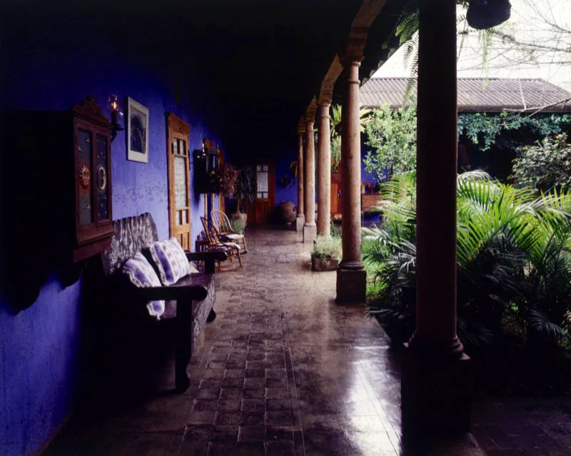 Casa antigüeña restaurada a comienzos del siglo XX, con piso en adoquín de cemento, clásicas columnas circulares de madera sobre pilastras de piedra y muebles pueblerinos.