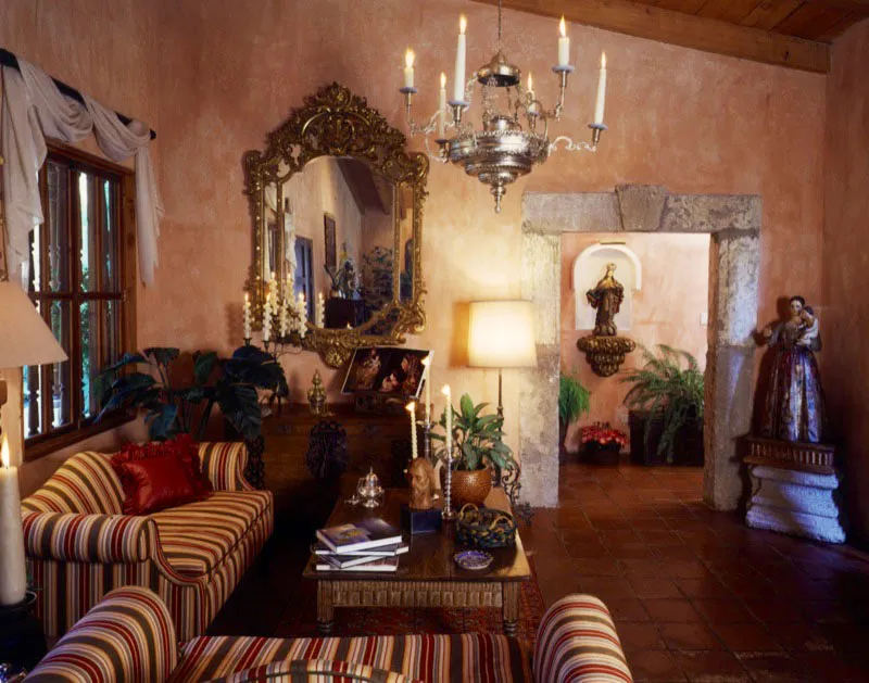 Sala de la casa, con un baúl colonial y un gran espejo rococó, al fondo. Tras el marco incorporado del vano, en piedra antigua, una escultura barroca guatemalteca estofada de la Virgen sobre una peana dorada, y a la derecha, dentro del salón, otra escultura mariana en madera policromada con el niño. De la techumbre cuelga una lámpara de plata colonial. En la mesa, unos candeleros y un incensario también de plata.